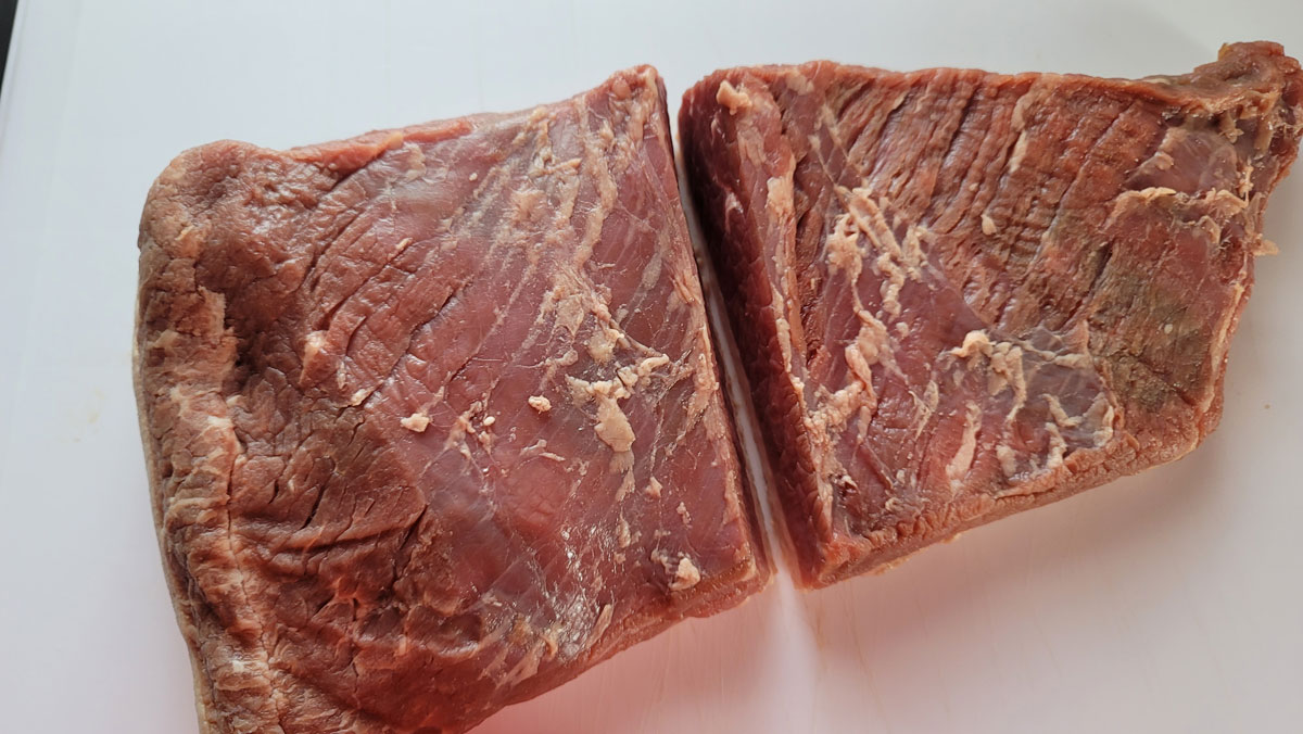 Brisket on a cutting board, cut in half.