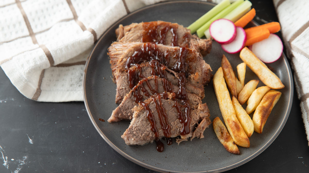 Sliced brisket on a gray plate drizzled with BBQ sauce.