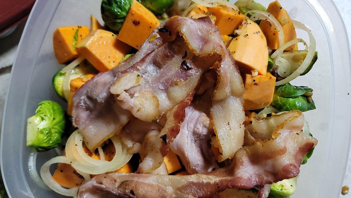 Vegetables in a container with bacon on top, to store and cook the next day.