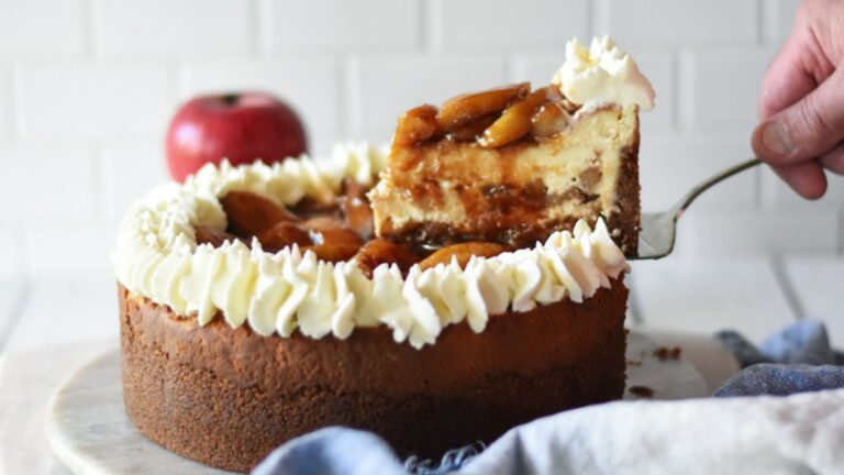 Slice of caramel apple cheesecake lifting from the whole cake.