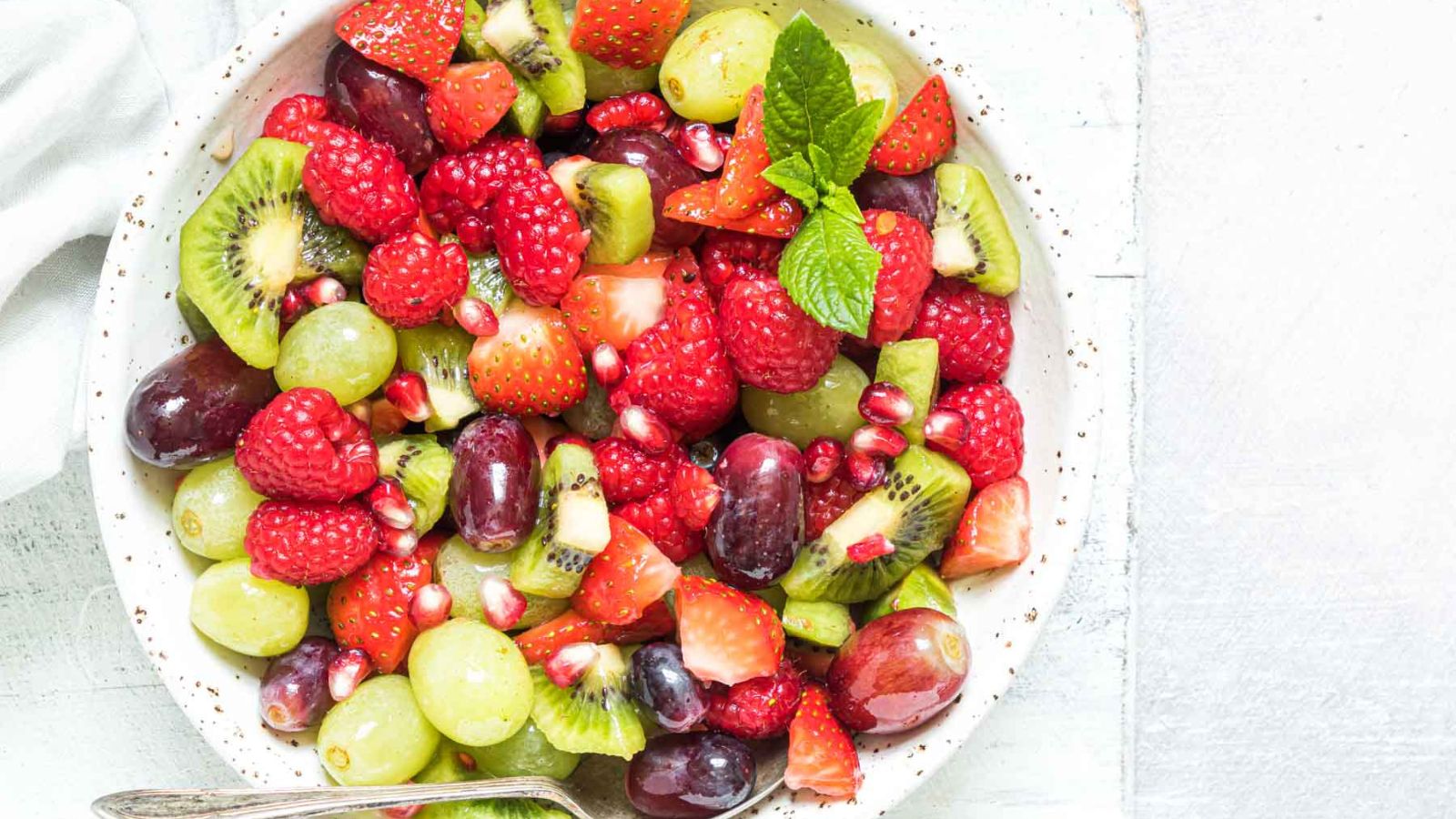Colorful fruit salad in a white bowl garnished with mint.