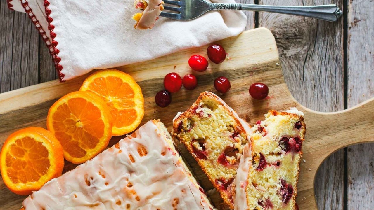 Slices of cranberry quick bread with orange slices on a cutting board.