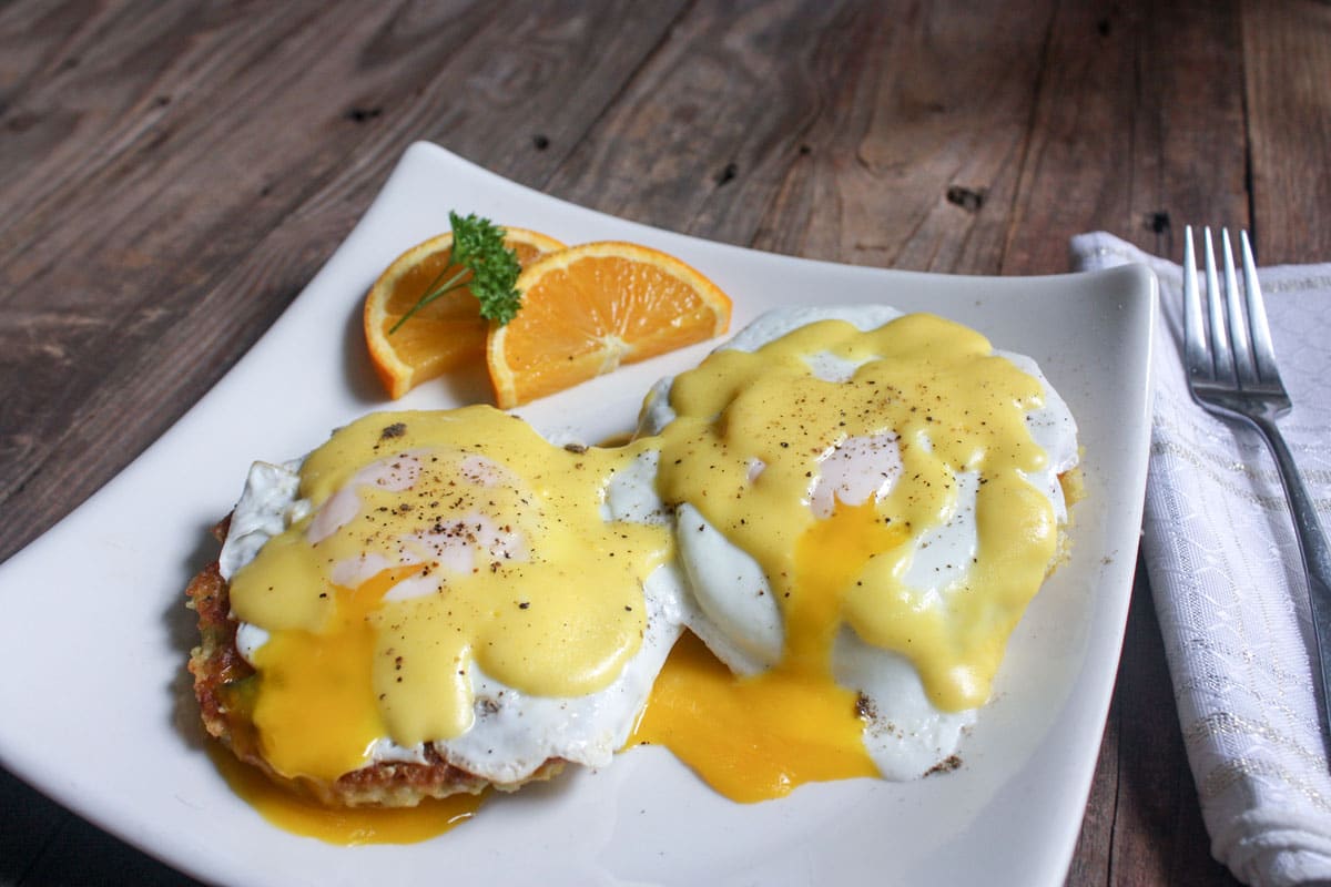Eggs Benedictwith broken yolks on white plate