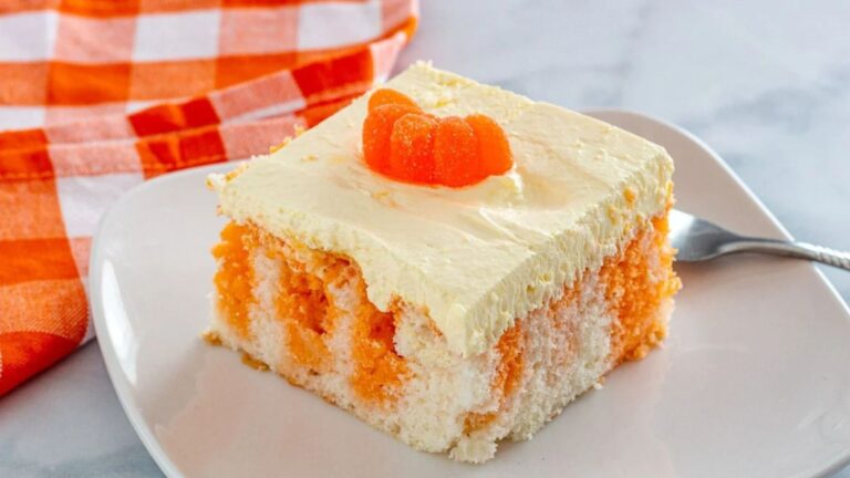 Slice of orange and white cake with an orange candy on top.
