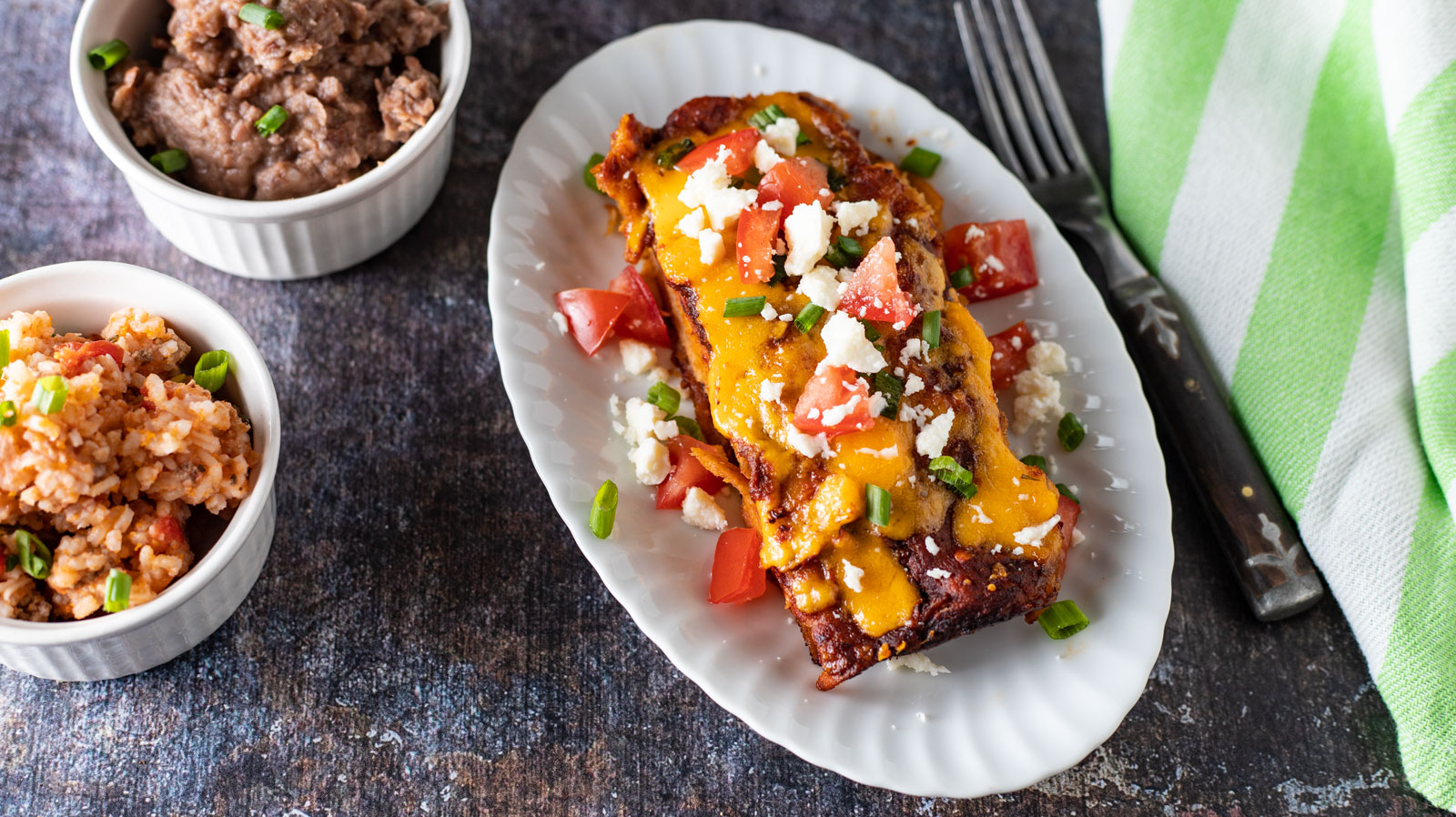 Two enchiladas on white plate with side dishes.