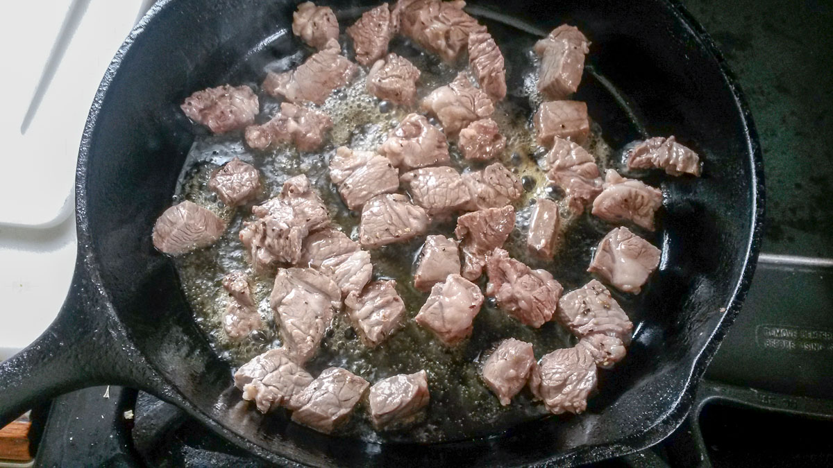 Venison chunks browning in a skillet.