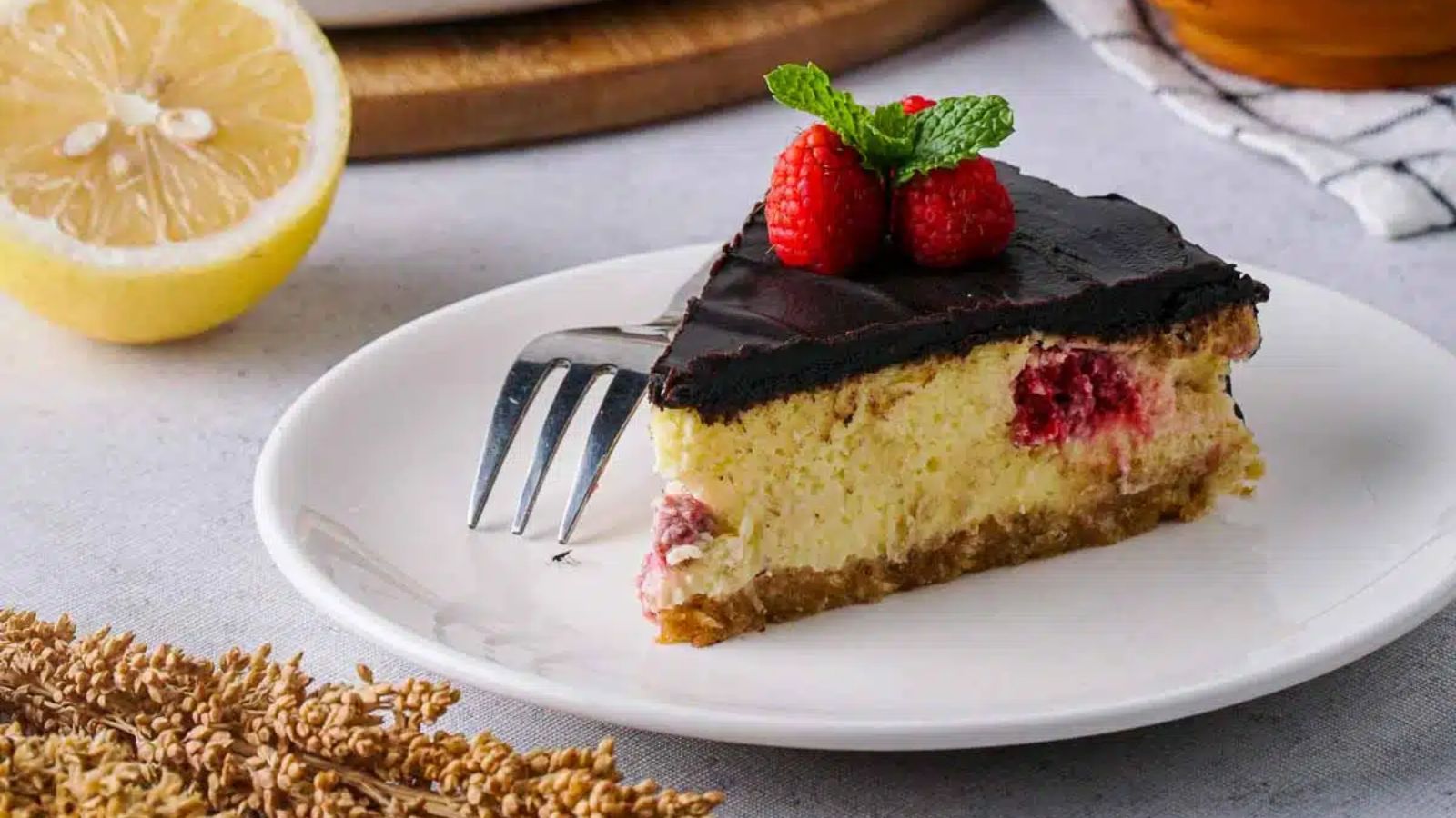 A slice of chocolate cake with raspberry on top on a plate.