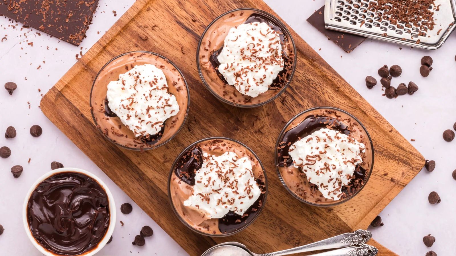Four glasses of chocolate mousse on a wooden board.