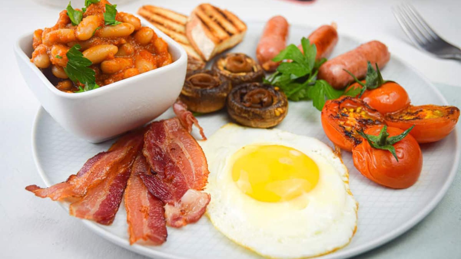 Egg, bacon, tomatoes, mushrooms, sausages, breads and beans on a plate.
