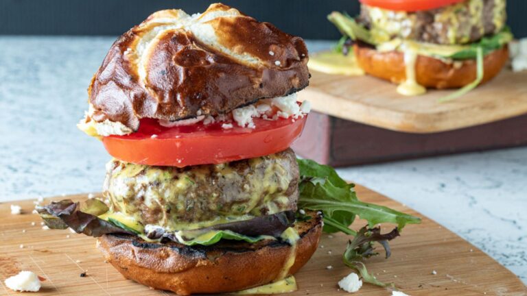 Juicy lamb burger on pretzel bun on wooden cutting board.