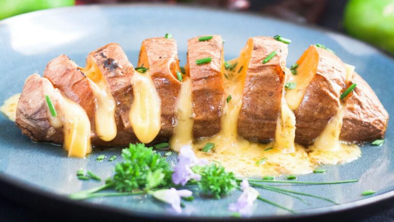 Cheesy hasselback sweet potato on blue plate.