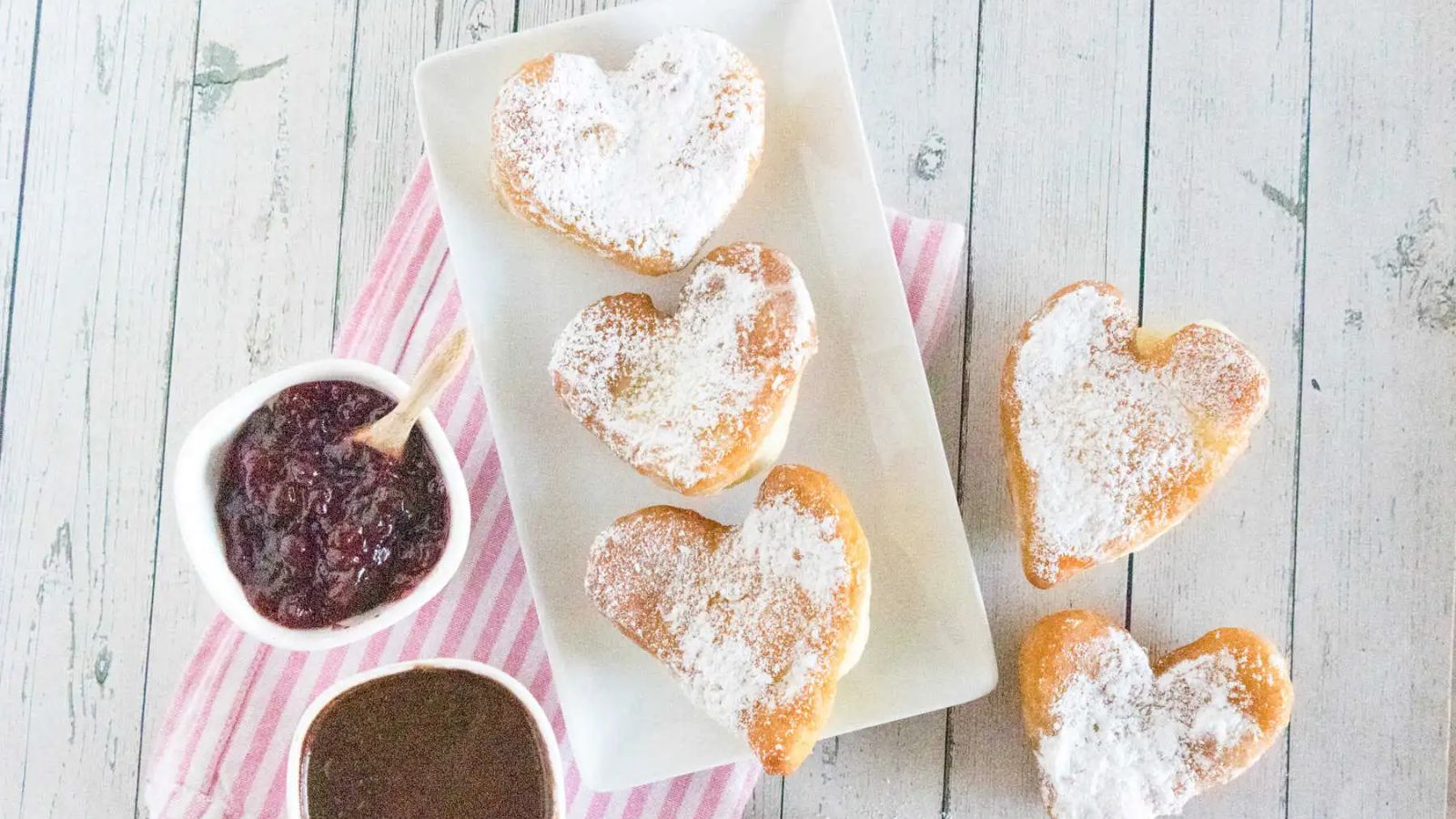 Heart beignets on a plate with chocolate sauce on the side.