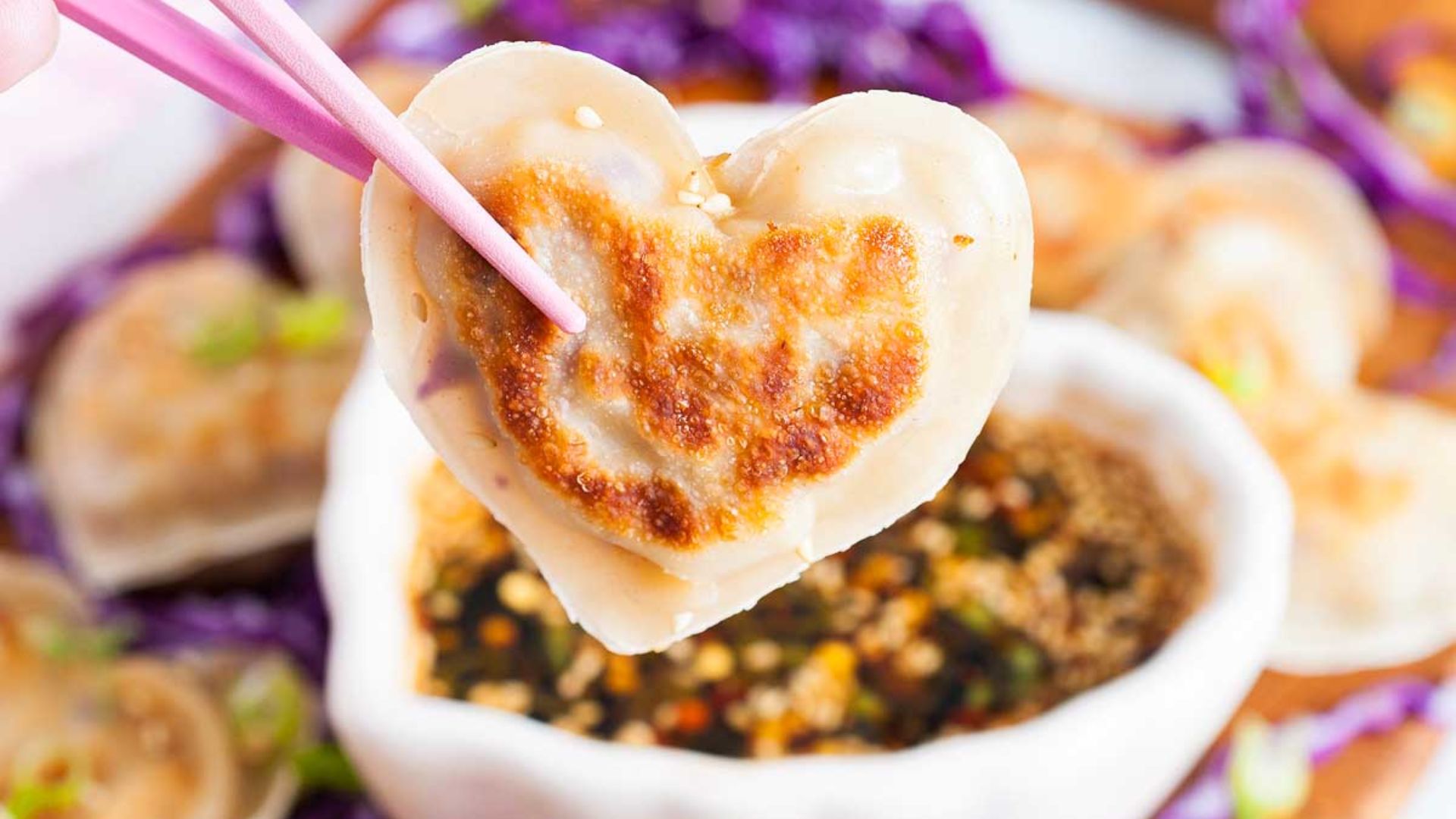 Heart shaped pork potstickers being hold by a chopsticks.