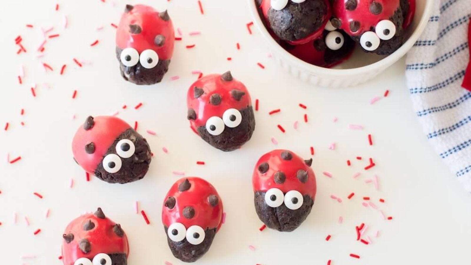 Ladybug oreo truffles with sprinkles on a white surface.