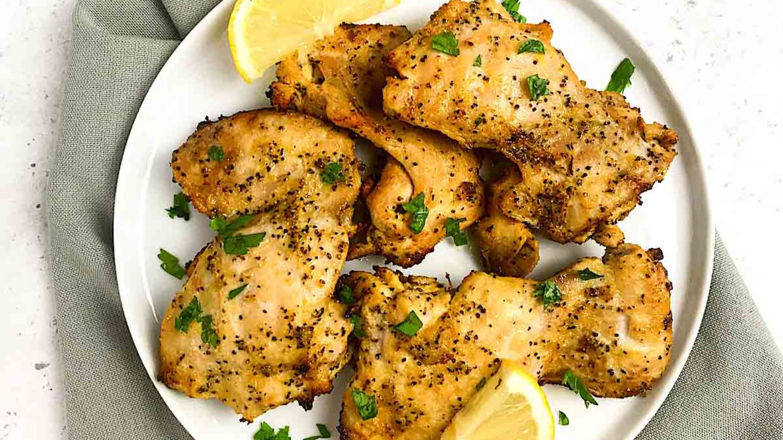 Chicken thighs on a plate with sliced lemons.