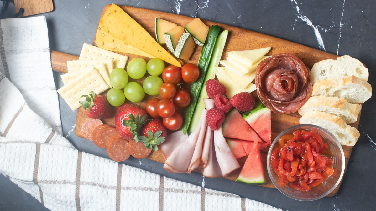 Charcuterie board for two with meat, cheese and colorful fruit.