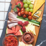 Mixed cheeses, meat, fruit and veggies on a small board.