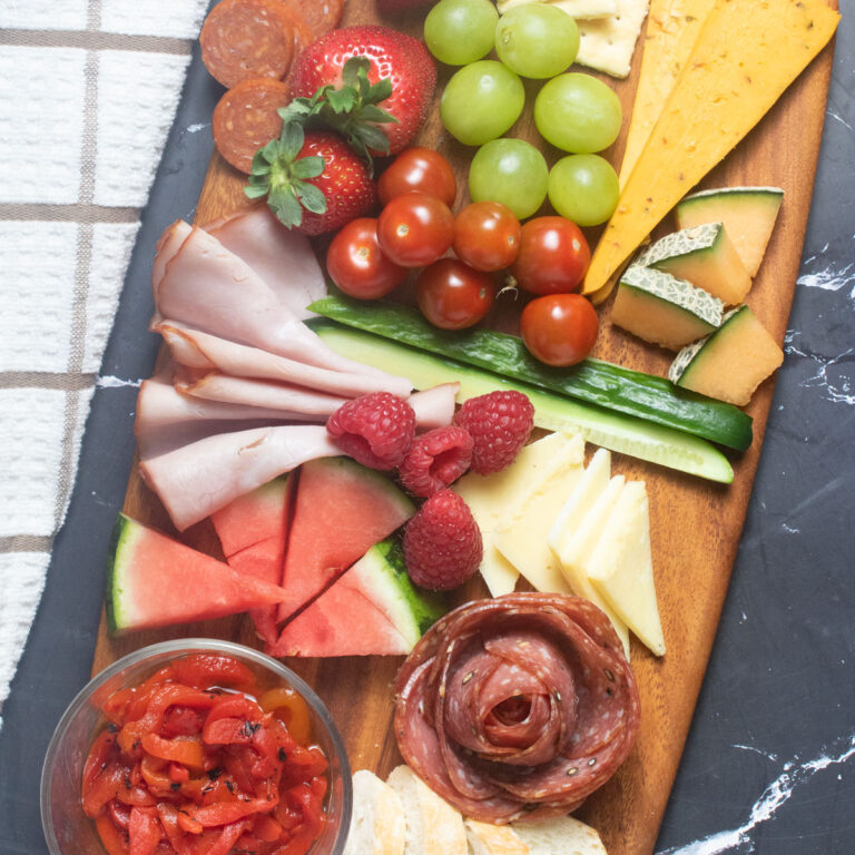 Mixed cheeses, meat, fruit and veggies on a small board.