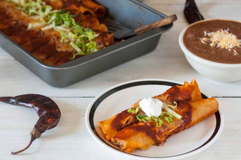 2 chicken enchiladas on white plate with black rim garnished with Mexican crema and lettuce