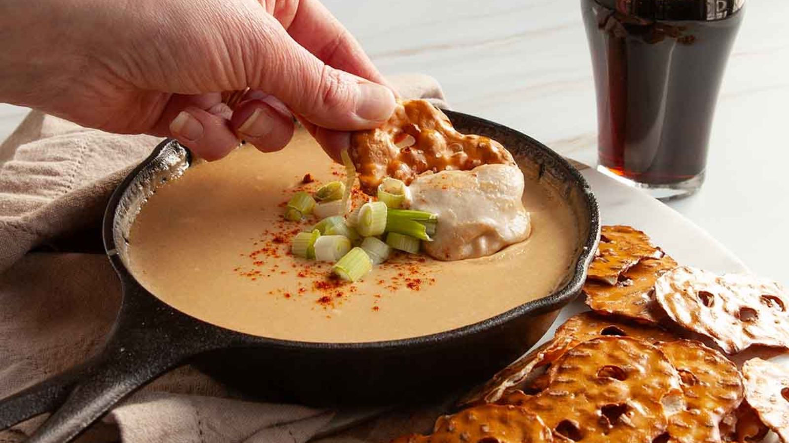 A hand dipping in the cheese sauce.