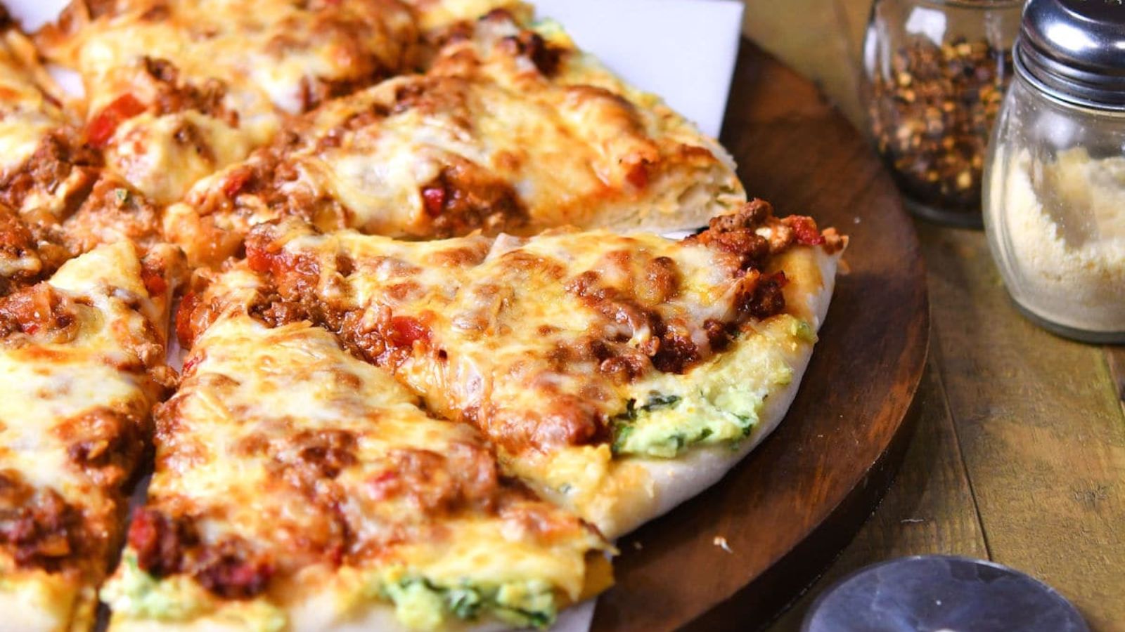 Slices of lasagna pizza on a wooden board.