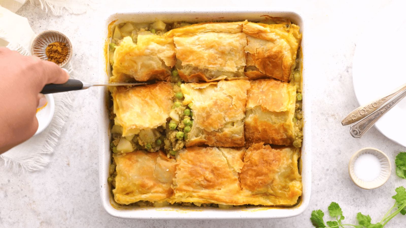 A hand slicing samosa pie on a tray.