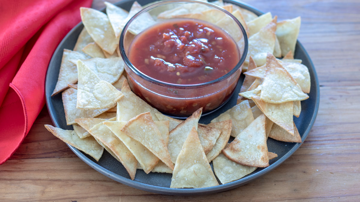 Tortilla chips surrounding a bowl of salsa on a gray plate.