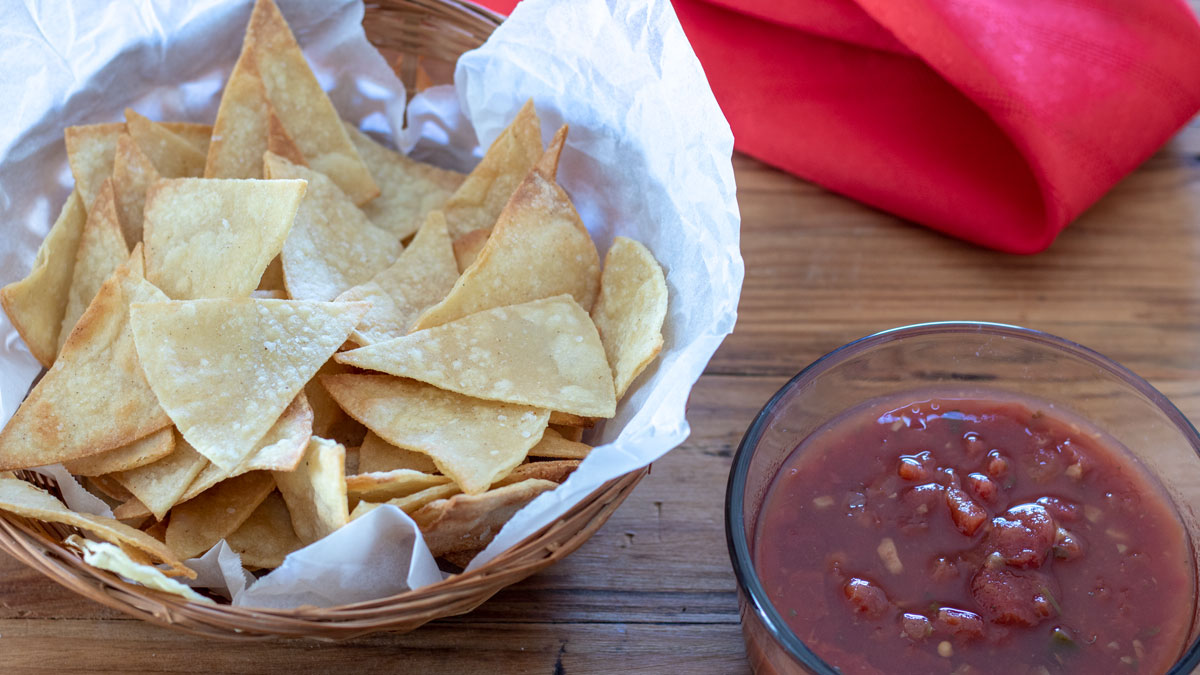 Tortilla chips in a basket next to a bowl of salsa.