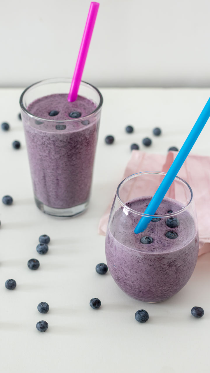 Blueberry smoothie in round glass with blue straw.