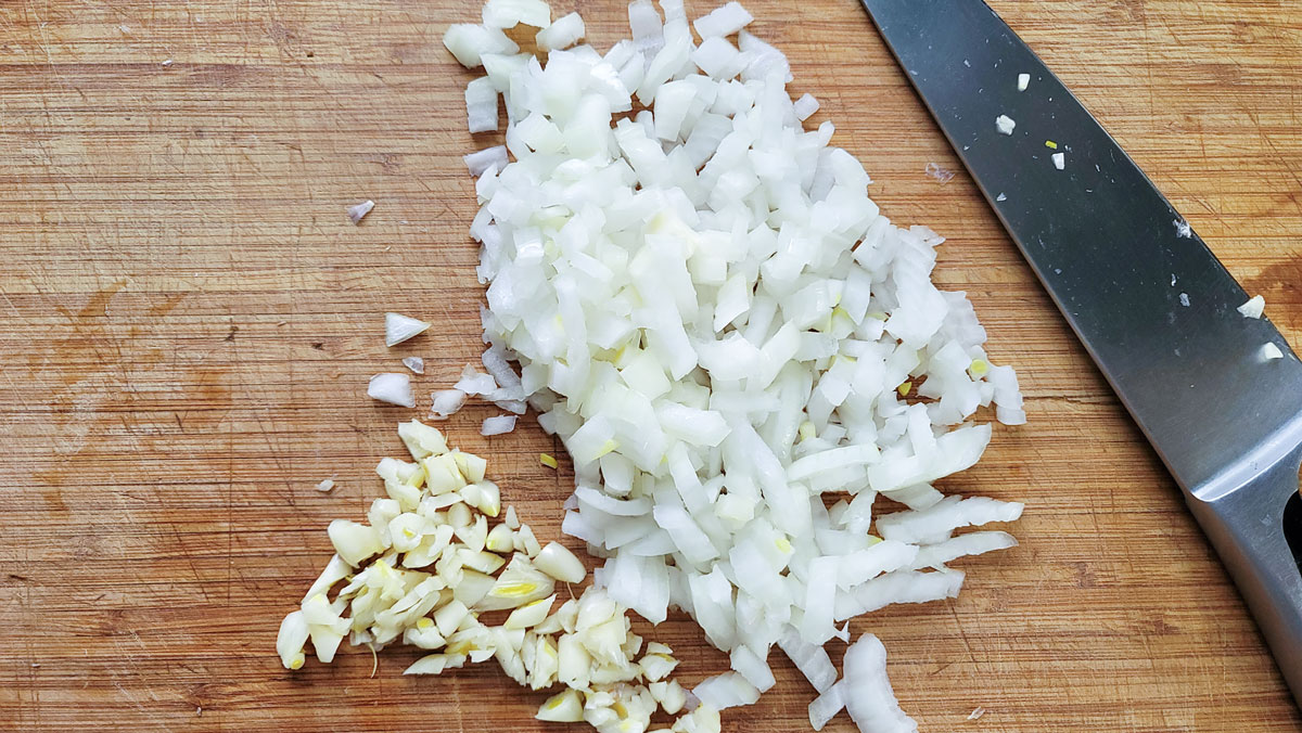 Chopped onion and garlic on a cutting board.