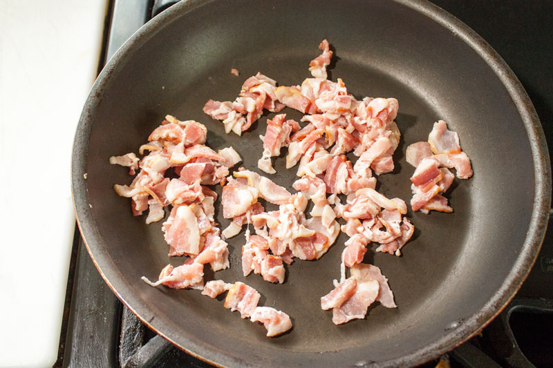 Crisping pieces of bacon in a skillet.
