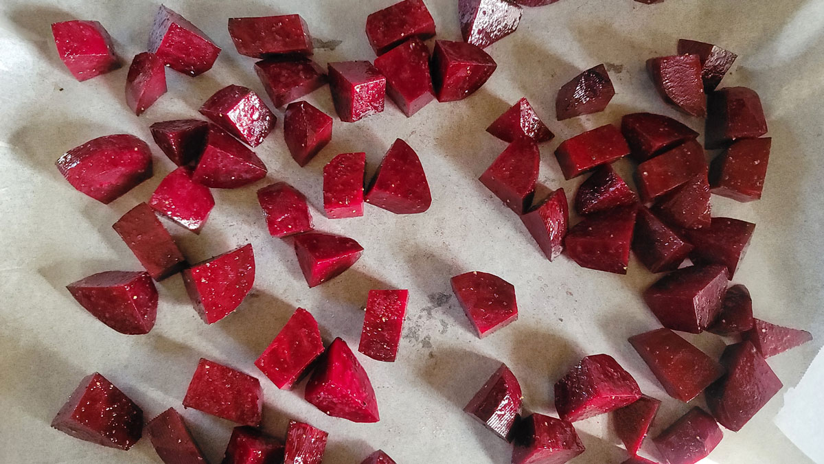 Beet chunks spread out on a parchment covered baking sheet.