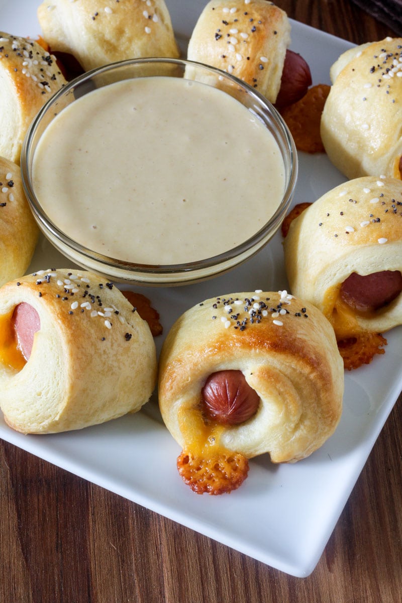 cheesy hot dogs wrapped in crescent roll dough with honey mustard dipping sauce on white plate