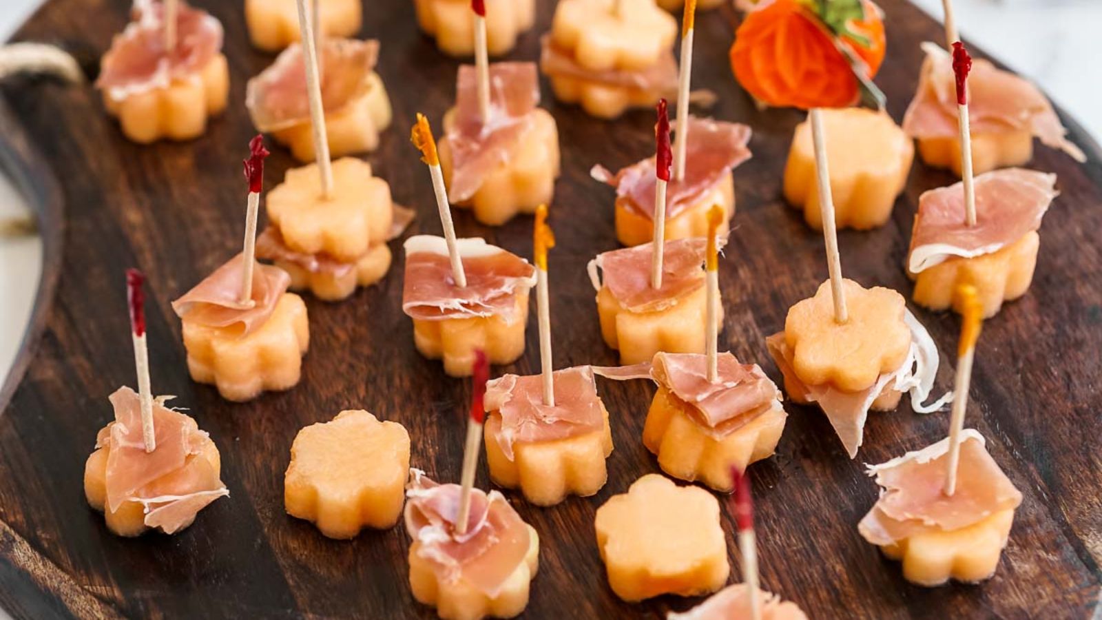 Prosciutto and melon bites on a wooden board.