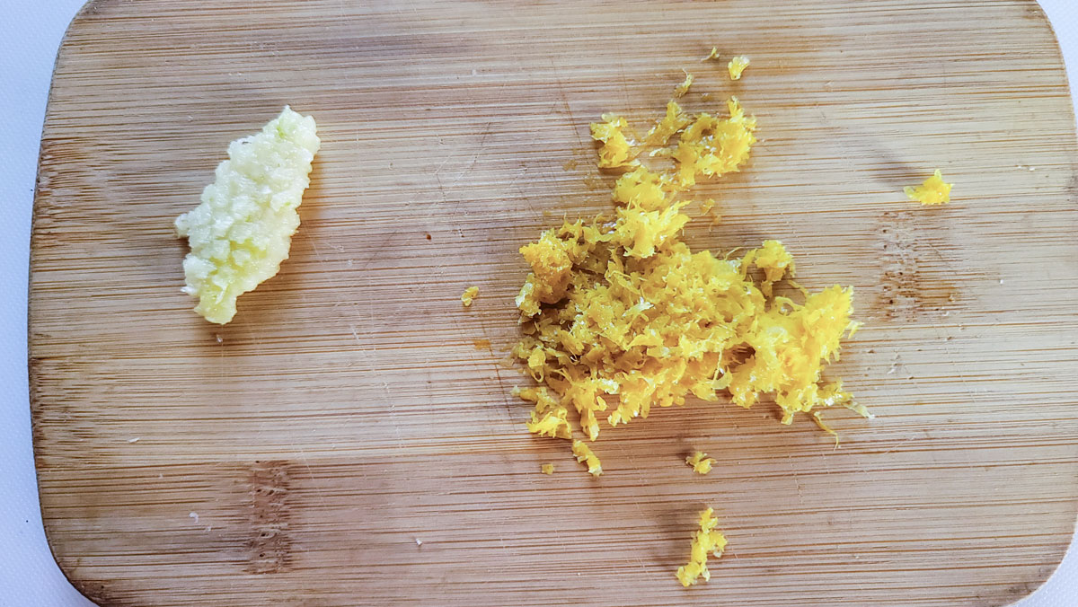 Lemon zested and grated garlic on a wooden board.