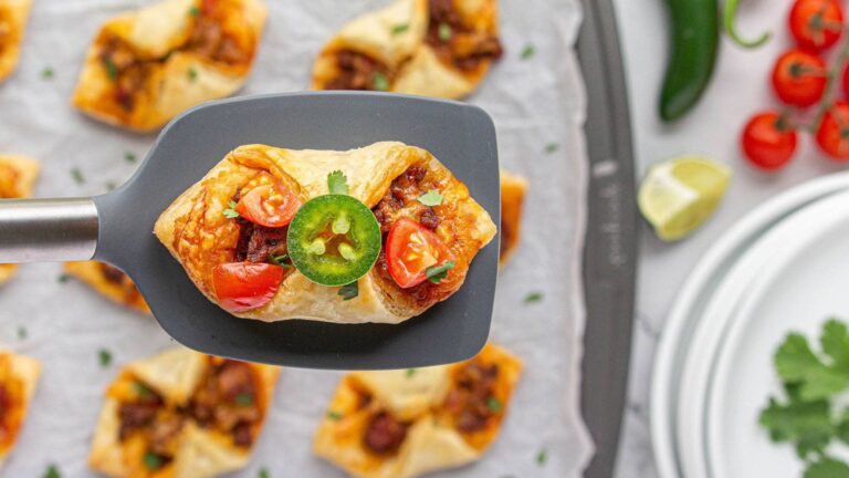 Puff pastry taco on a spatula held above more tacos.