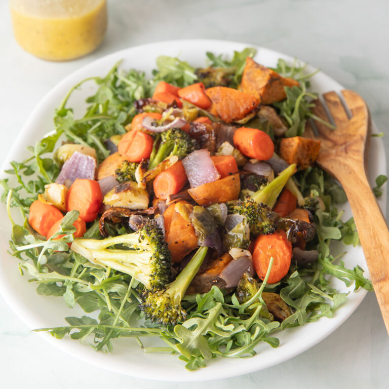Platter filled with roasted vegetable salad on a bed of arugula.