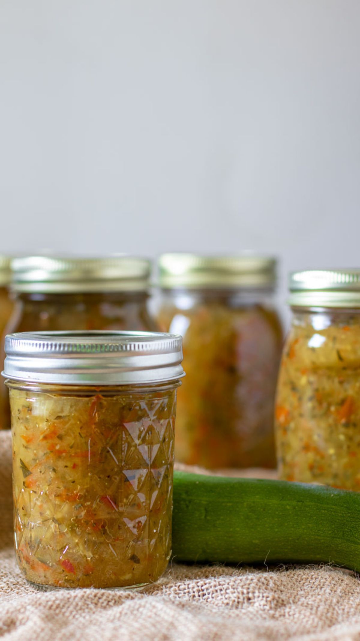 Group of jars filled with zucchini relish with a fresh zucchini.
