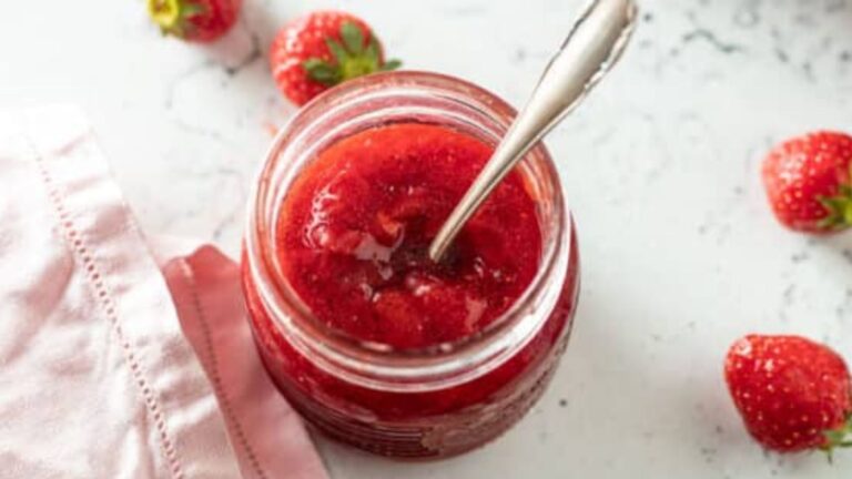 Spoon resting in jar of strawberry jam.