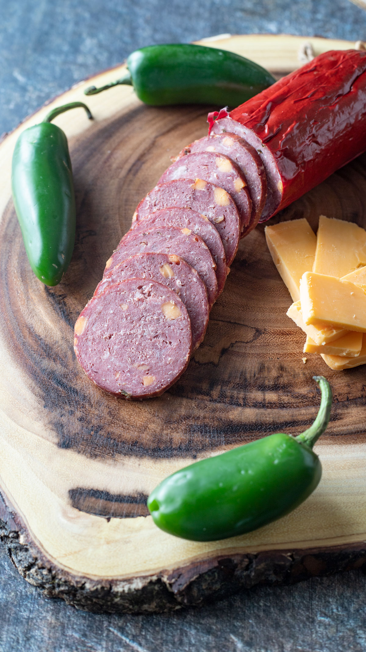 Sliced venison summer sausage on a wooden slab with jalapeños.
