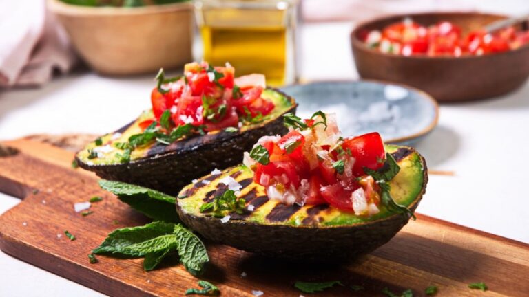Grilled stuffed avocado with vegetable on top on a wooden board.