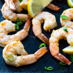 Air fried shrimp on a black board garnished with chives and lemon wedges.