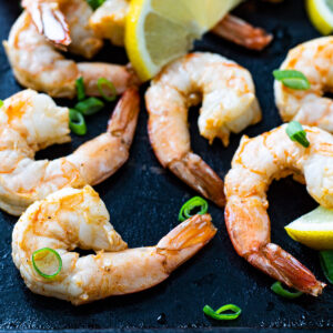 Air fried shrimp on a black board garnished with chives and lemon wedges.