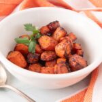 White bowl with golden roasted carrots garnished with fresh parsley.