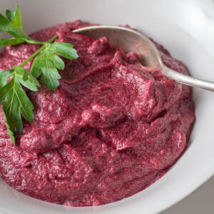 Pink beet puree in a white bowl garnished with parsley.