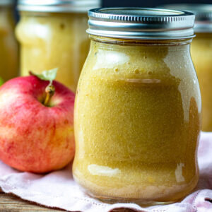 Jars of applesauce with a red apple.