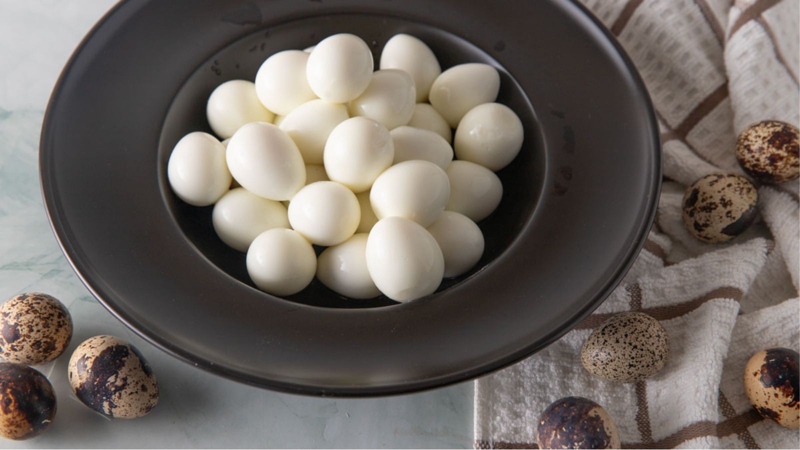 Black bowl filled with hard boiled quail eggs.