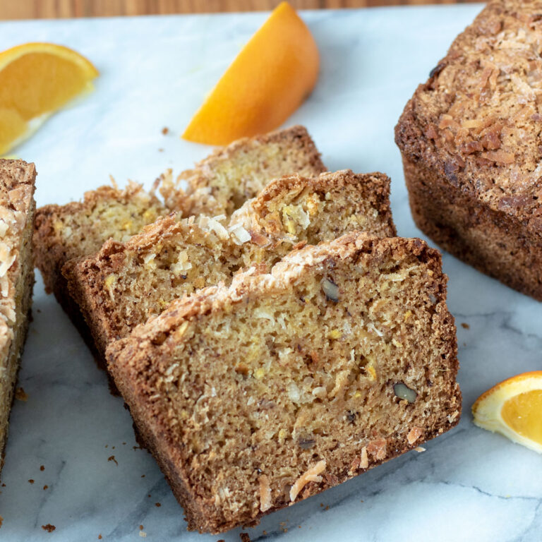 Slices of orange pineapple quick bread on a marble board with orange wedges.
