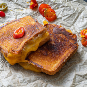 Two grilled cheese sandwiches topped with candied jalapenos.
