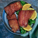 Chunks of smoked steelhead trout garnished with greens and orange wedges.